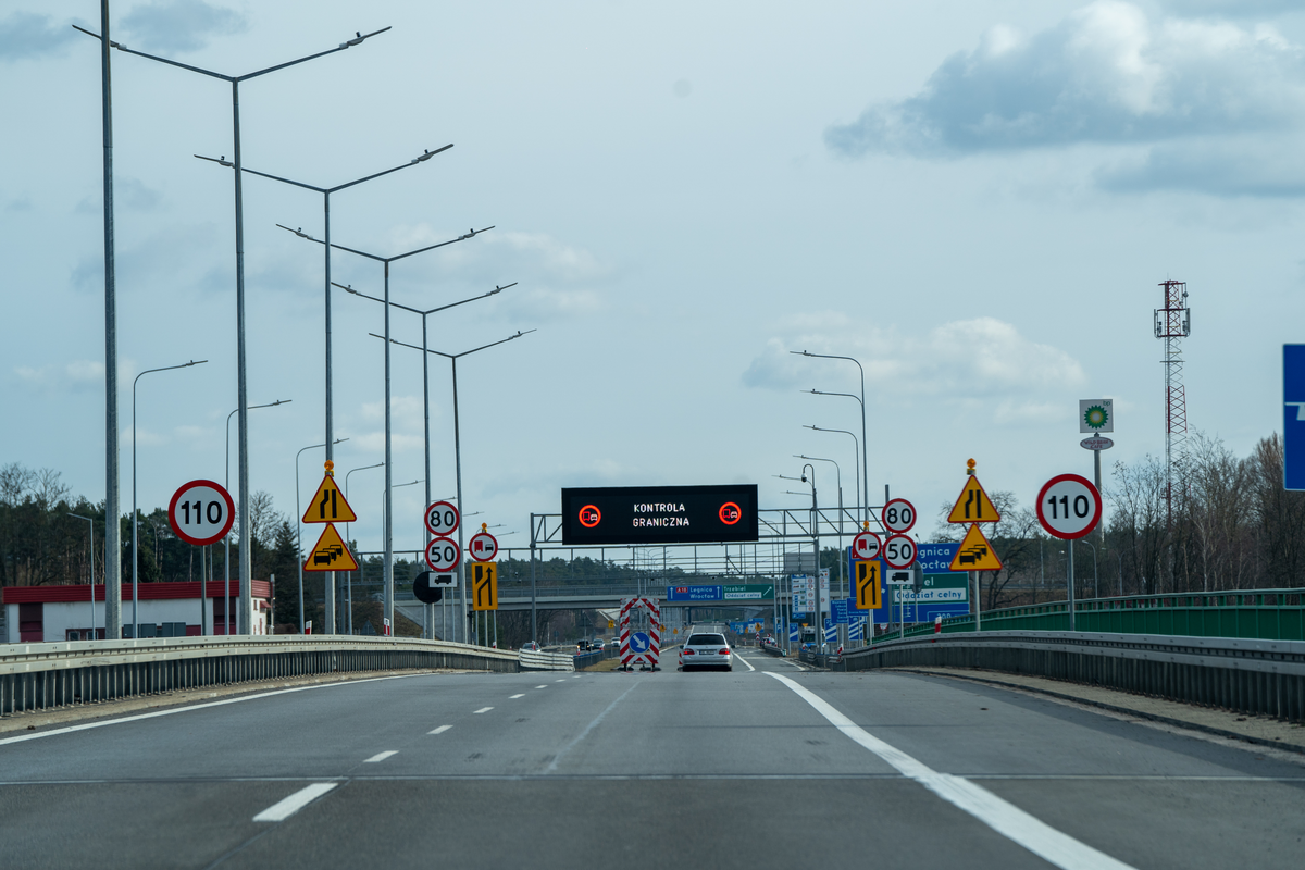 View through windshield crossing the German-Polish border on the A18 motorway, showing the abrupt transition from smooth asphalt to older concrete slab road surface
