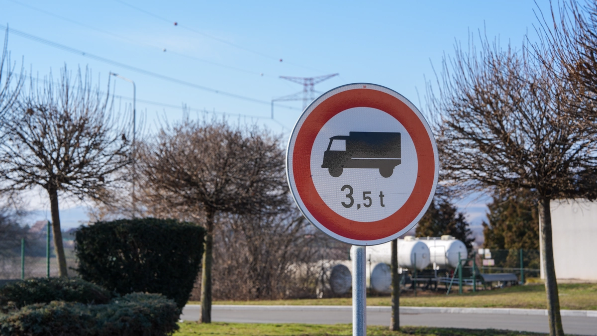 Czech 3.5 tonne weight restriction road sign with HGV pictogram in a red circle, mounted at a roadside with bare winter trees, electricity pylons and propane storage tanks in the background, February 2026