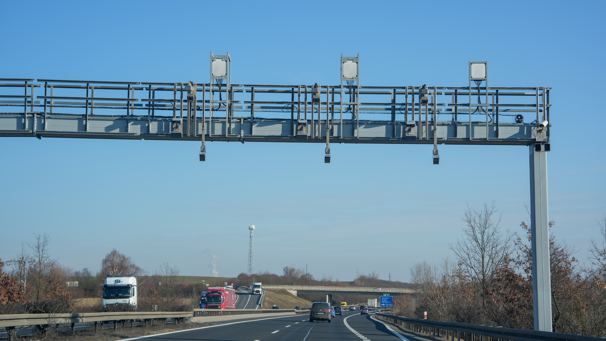 Czech D6 motorway vignette enforcement gantry with multiple cameras and sensors spanning full carriageway with trucks and cars passing underneath against clear blue sky, February 2026