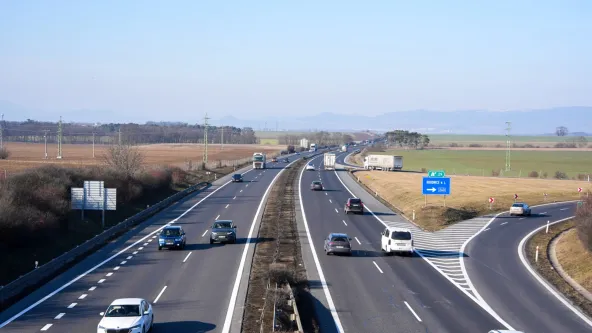 Czech D8 motorway traffic near Roudnice nad Labem exit 29, cars and trucks on both carriageways across open farmland toward distant hills