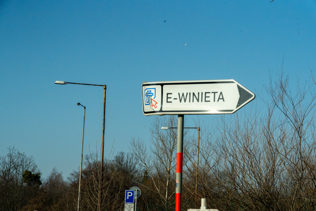 Biała tablica kierunkowa z czerwoną strzałką wskazującą punkt sprzedaży e-winiety, z napisem po polsku („E-WINIETA