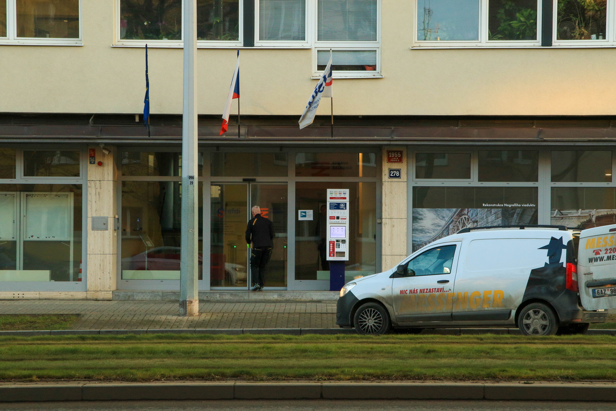 Edalnice.cz Czech e-vignette self-service kiosk installed outside SFDI/SŽDC office building at Prague Libeň 1955/278 with Czech, EU and operator flags, a worker entering the building and a white Messenger Dacia delivery van parked in front, December 2025