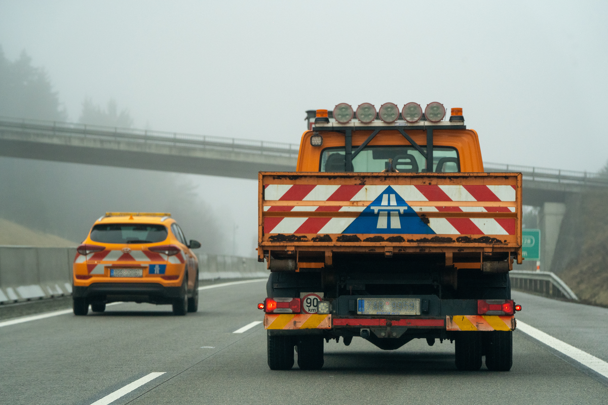 Czech road maintenance service vehicles on D5 motorway in foggy winter weather, including orange Hyundai patrol SUV with red and white chevrons and orange ŘSD utility truck displaying Czech motorway symbol on tailgate, both vignette-exempt service vehicles, February 2026