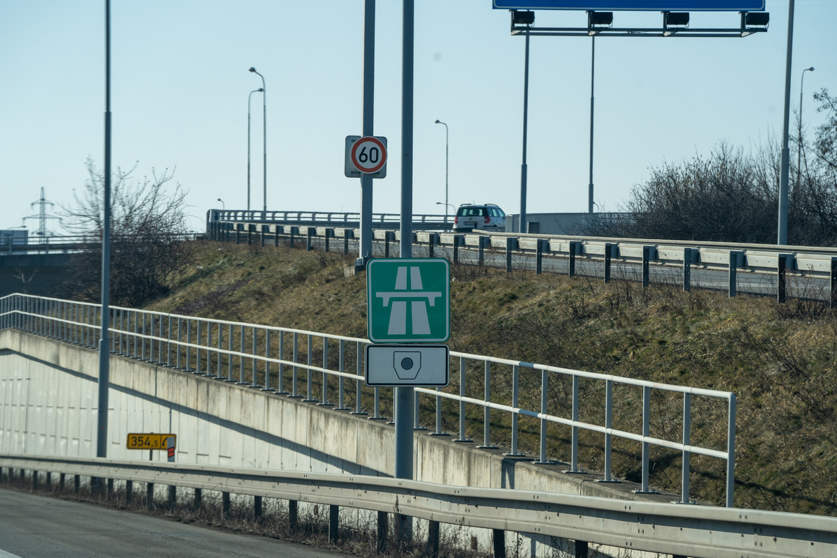 Czech green motorway sign with vignette pictogram below it on a slip road joining the D1 motorway near km 354.5, with 60 km/h speed limit on the approach, marking the start of the vignette obligation zone, February 2026