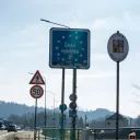 Blue EU-style "Česká republika" border entry sign covered in travel stickers next to white oval Czech coat of arms sign at the Náchod–Kudowa-Zdrój crossing on the E67/I/33 between Czech Republic and Poland
