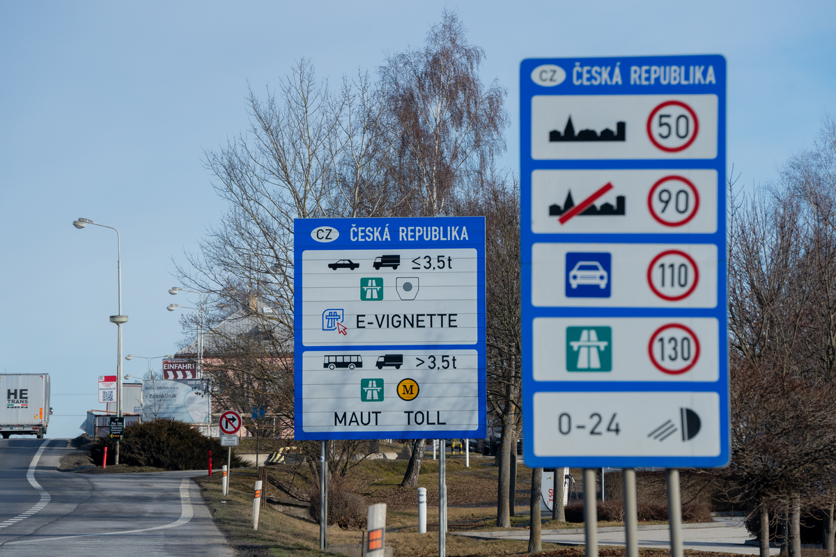 Czech Republic border information signs at the Dolní Dvořiště crossing from Austria, showing speed limits (50, 90, 110, 130 km/h) with 0-24h dipped headlights rule and a separate sign with e-vignette obligation for vehicles up to 3.5t and MAUT/TOLL for vehicles over 3.5t, on the E55 Linz–Prague corridor, February 2026