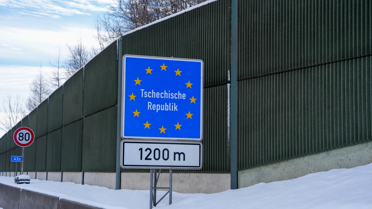 EU-style Tschechische Republik border sign 1200m ahead alongside an 80 km/h speed limit sign for vehicles with trailers, snow-covered noise barriers on the A17/D8 corridor approaching the Czech border, winter scene, February 2026