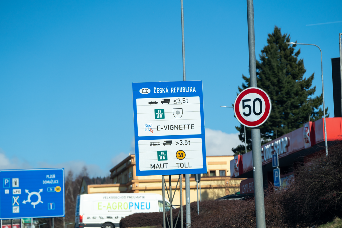 Czech Republic blue roadside information sign showing e-vignette requirement for vehicles ≤3.5t and MAUT/TOLL system for vehicles >3.5t, with Plzeň/Domažlice direction sign and 50 km/h speed limit visible, D5 motorway corridor near German border, February 2026
