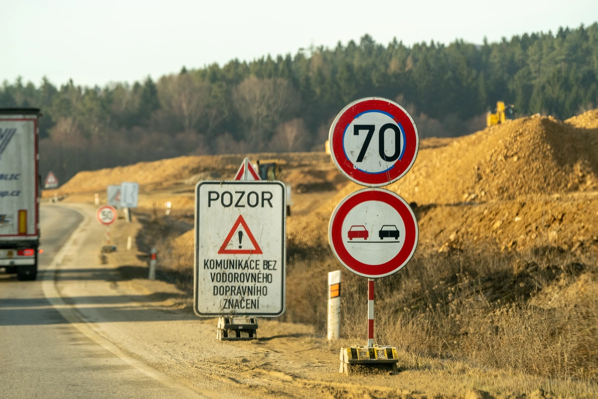 Czech roadworks warning signs at active construction site with 70 km/h speed limit, no overtaking circle and POZOR ('caution — road without horizontal markings') sign in Czech, white truck and earthworks visible alongside the carriageway, February 2026
