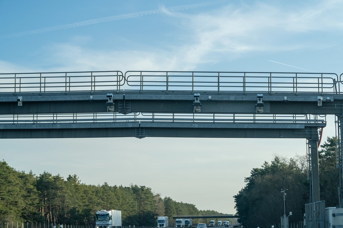 Czech vignette enforcement gantry spanning a motorway with multiple ANPR cameras and toll sensors mounted underneath, HGV traffic and pine forest below, late afternoon winter light, D2 corridor, February 2026