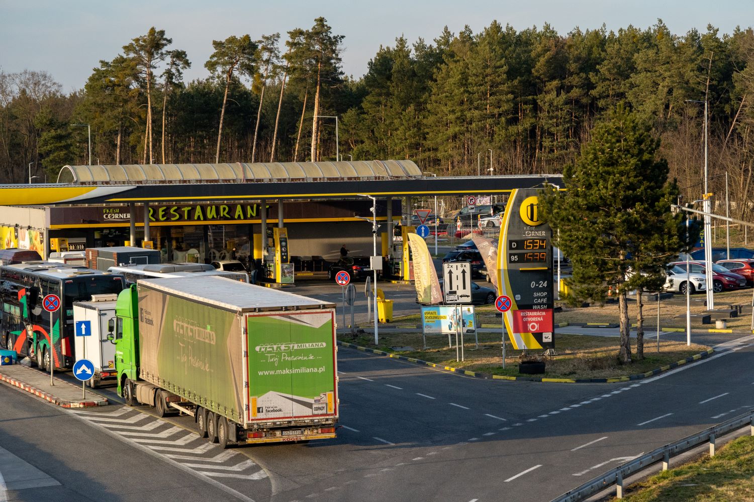 Slovnaft service station with a Fresh Corner restaurant in Slovakia, with trucks and coaches lined up at the pumps in low sunlight 