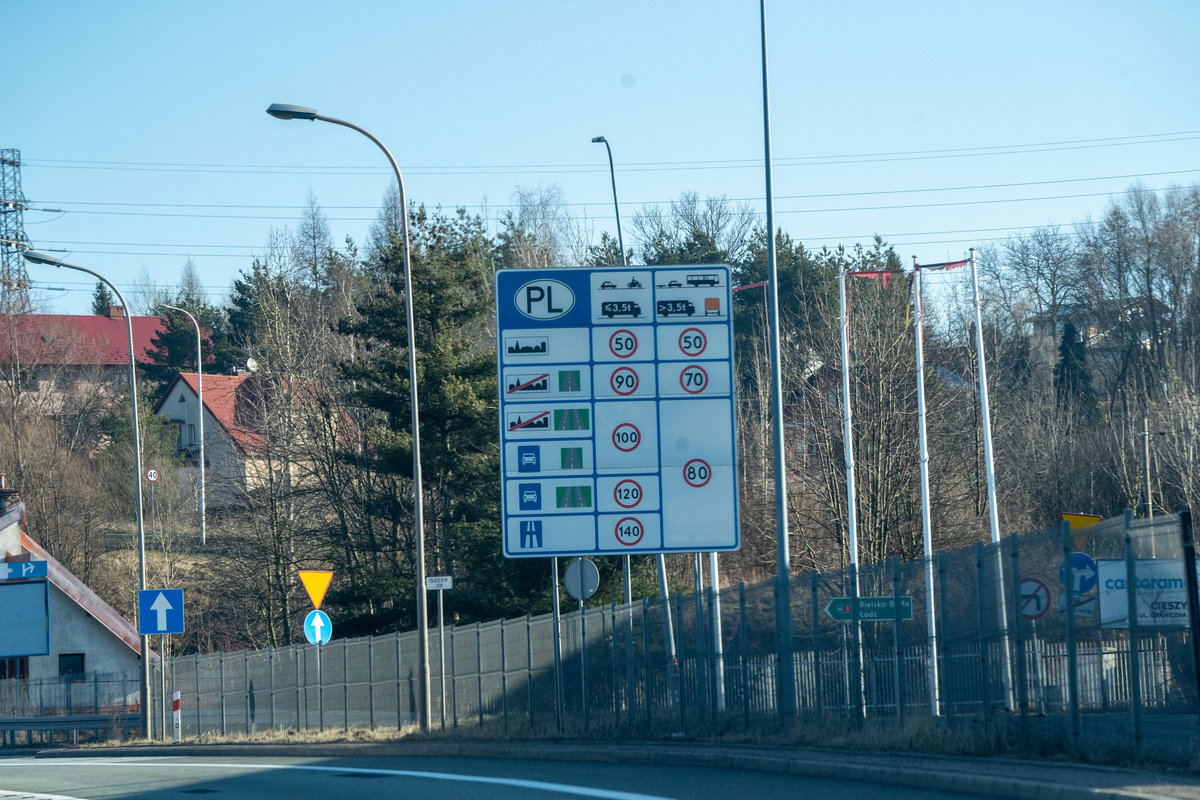 Polish speed limit information board at the Český Těšín–Cieszyn border crossing showing speed limits for vehicles up to 3.5t and over 3.5t in built-up areas, single carriageways, dual carriageways, expressways and motorways (50/90/100/120/140 km/h), with direction sign to Bielsko-Biała and Łódź visible, February 2026